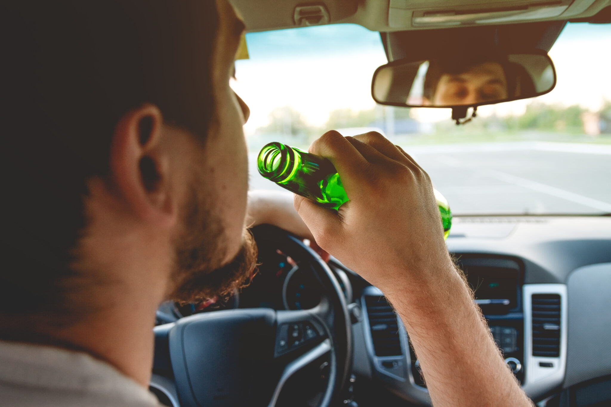 Drunk young man driving a car with a bottle of beer. St. Louis DWI Defense Attorneys